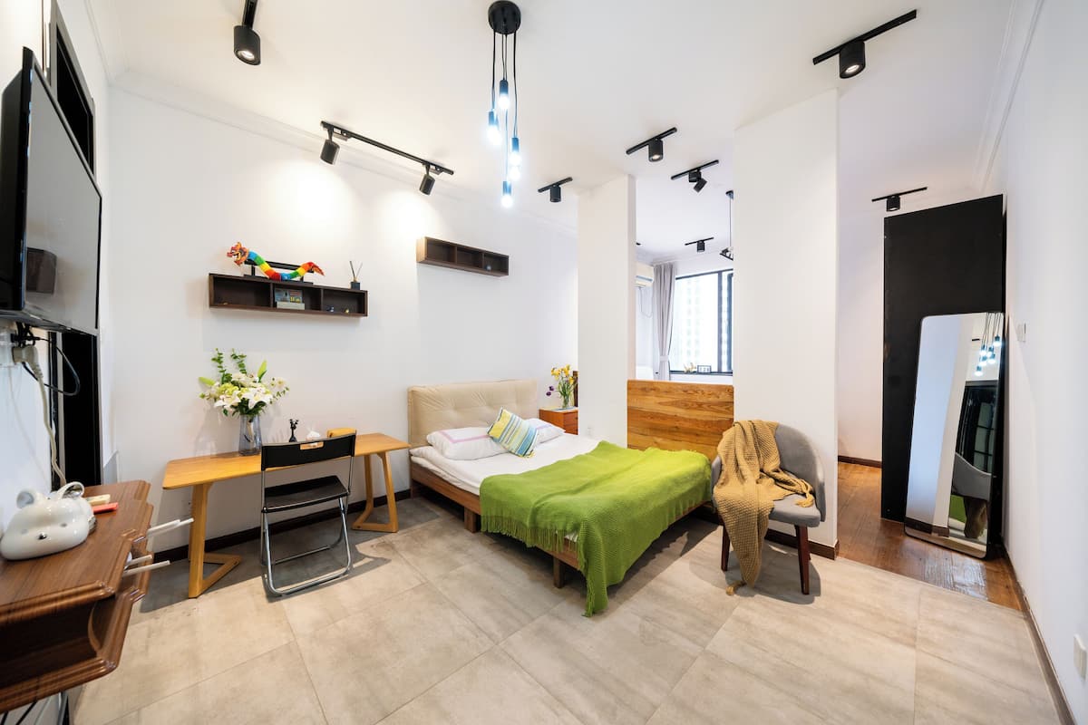 A modern bedroom with a bed, bedside table, chair, and a desk with a chair.