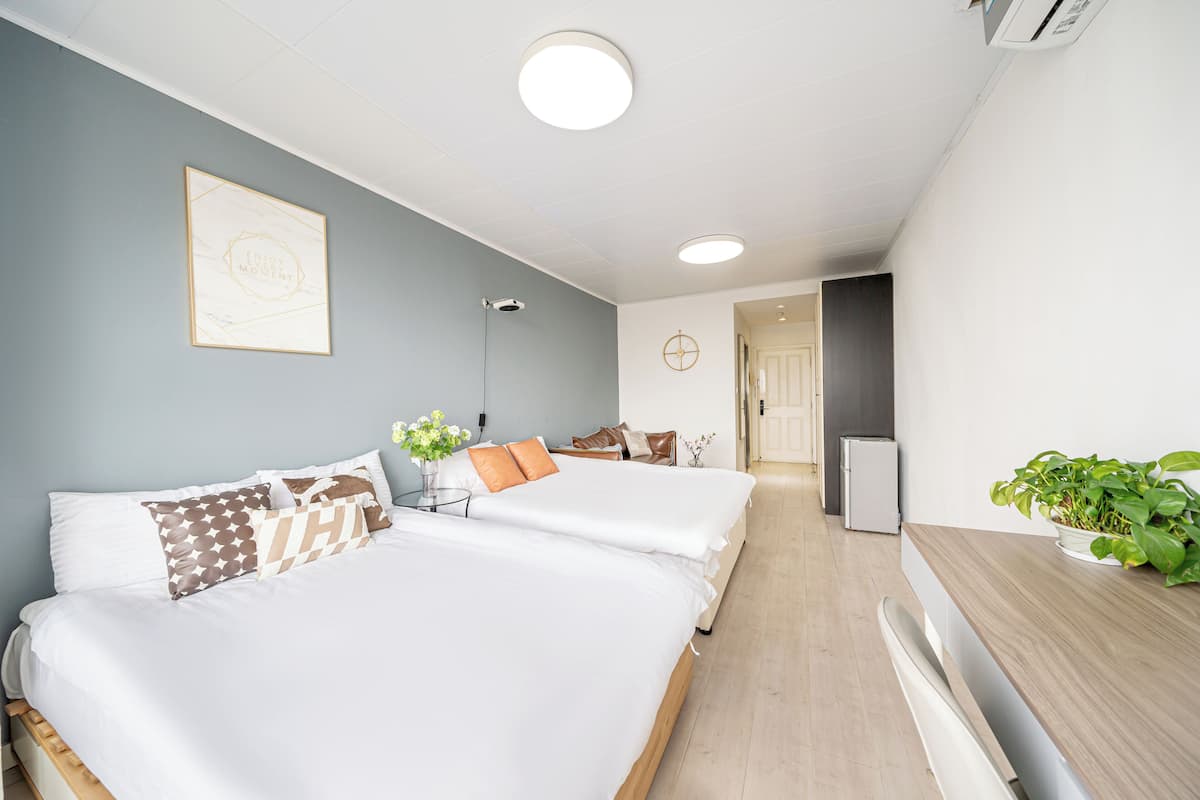 A modern hotel room with two beds, a small table, a refrigerator, and a potted plant.