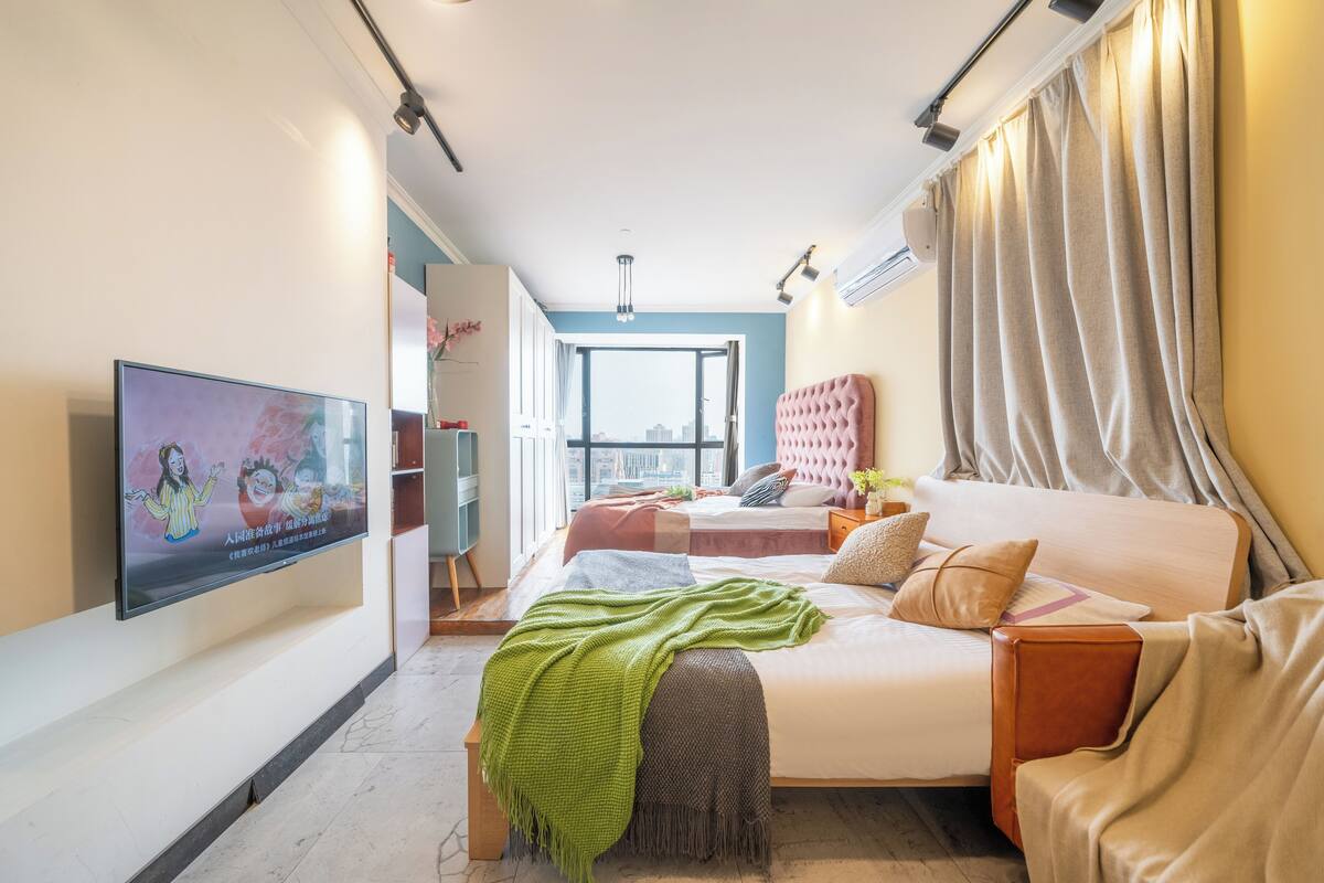 A modern hotel room with a large bed, a sofa, a TV, and a view of the city.