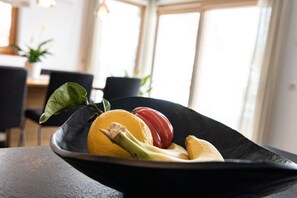 A black bowl on a table with a lemon, a red apple, and a banana.