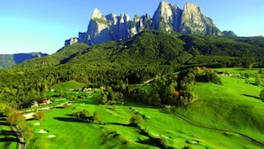 Un parcours de golf avec une chaîne de montagnes en toile de fond, entouré de forêts denses et de quelques bâtiments dispersés.