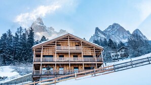 Un chalet en bois doté d’un balcon, situé au pied d’une montagne enneigée.
