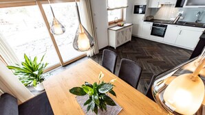 Une cuisine moderne avec des meubles blancs, une table à manger en bois et des luminaires suspendus.