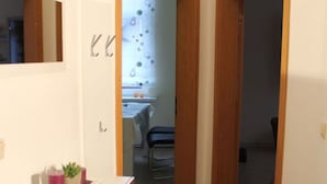 A narrow hallway with wooden flooring, a white cabinet with a plant, and a door leading to a room with a window and a chair. - 2 am Lustgarten Modern Retreat (Wernigerode)