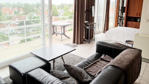 A modern hotel room with a balcony, a bed, a sofa, a small table, and a TV. - Apartment in Nieuwpoort for 4 Persons (Nieuwpoort)