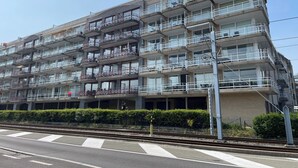 A multi-story building with balconies, a covered entrance, and a parking area in front. - Apartment in Nieuwpoort for 4 Persons (Nieuwpoort)