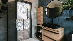 Un baño moderno con tocador de madera, un lavamanos negro y un espejo grande.