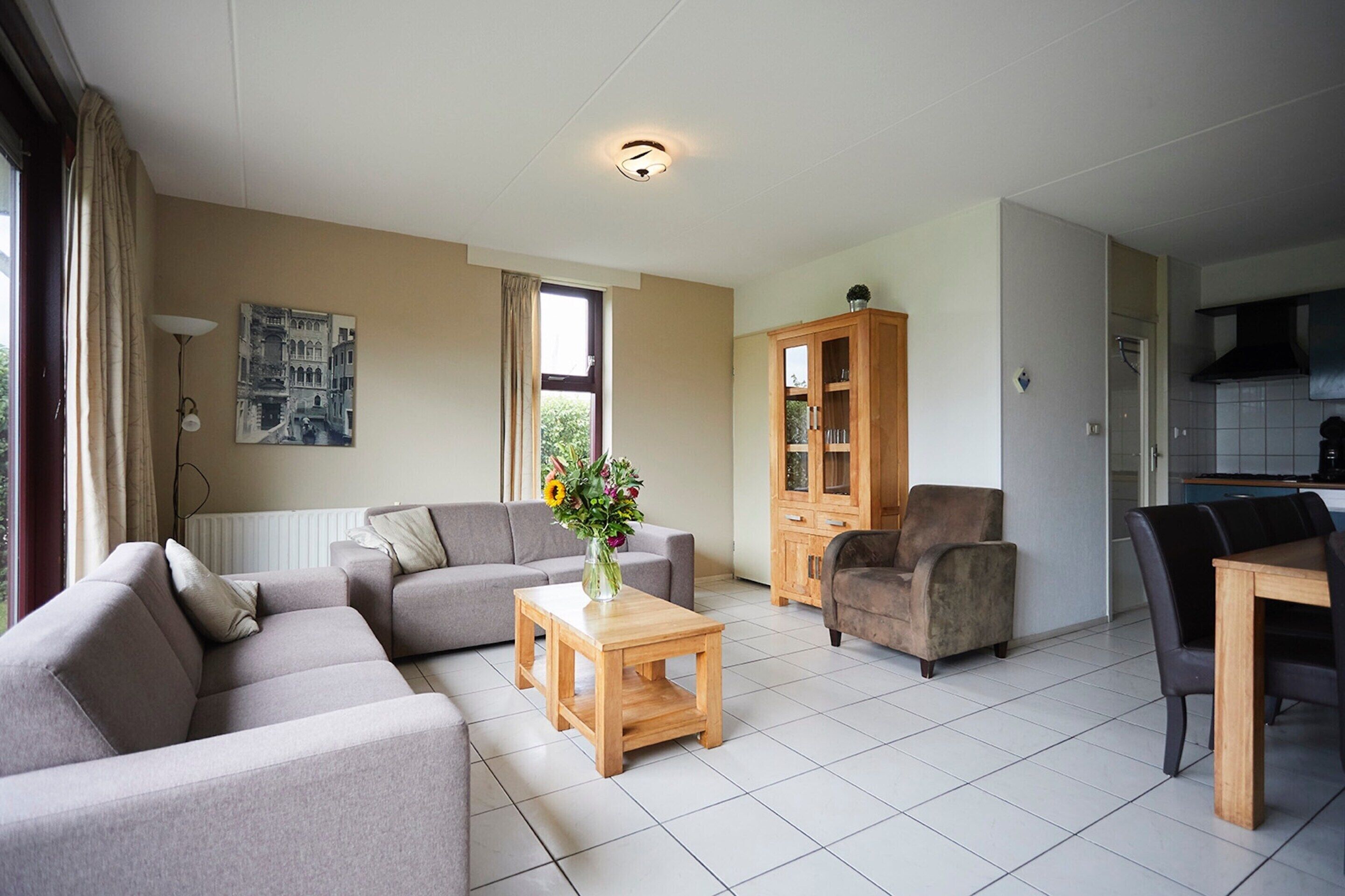 A living room with a sofa, a coffee table with a vase, a cabinet, and a dining area with chairs.