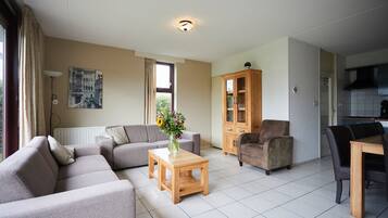 A living room with a sofa, a coffee table with a vase, a cabinet, and a dining area with chairs.