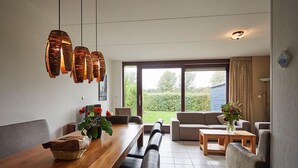 Een moderne eetruimte met een houten tafel, zwarte gewatteerde bankjes en een groot raam met uitzicht op het omliggende landschap.