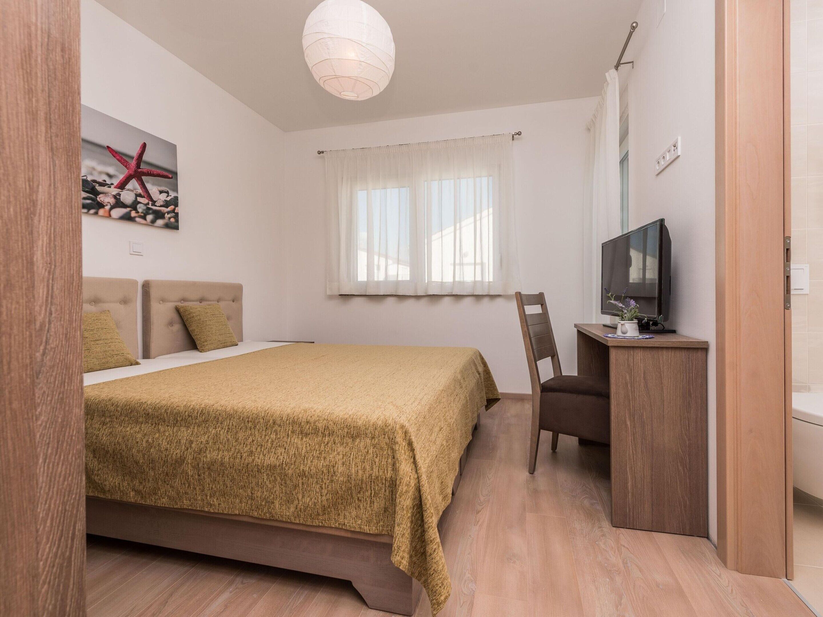 Een slaapkamer met een bed, een bureau met een televisie, een stoel en een raam met gordijnen.