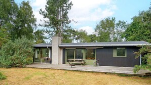 A two-story house with a deck, outdoor seating, and a chimney. - 5 Person Holiday Home in Melby (Melby)