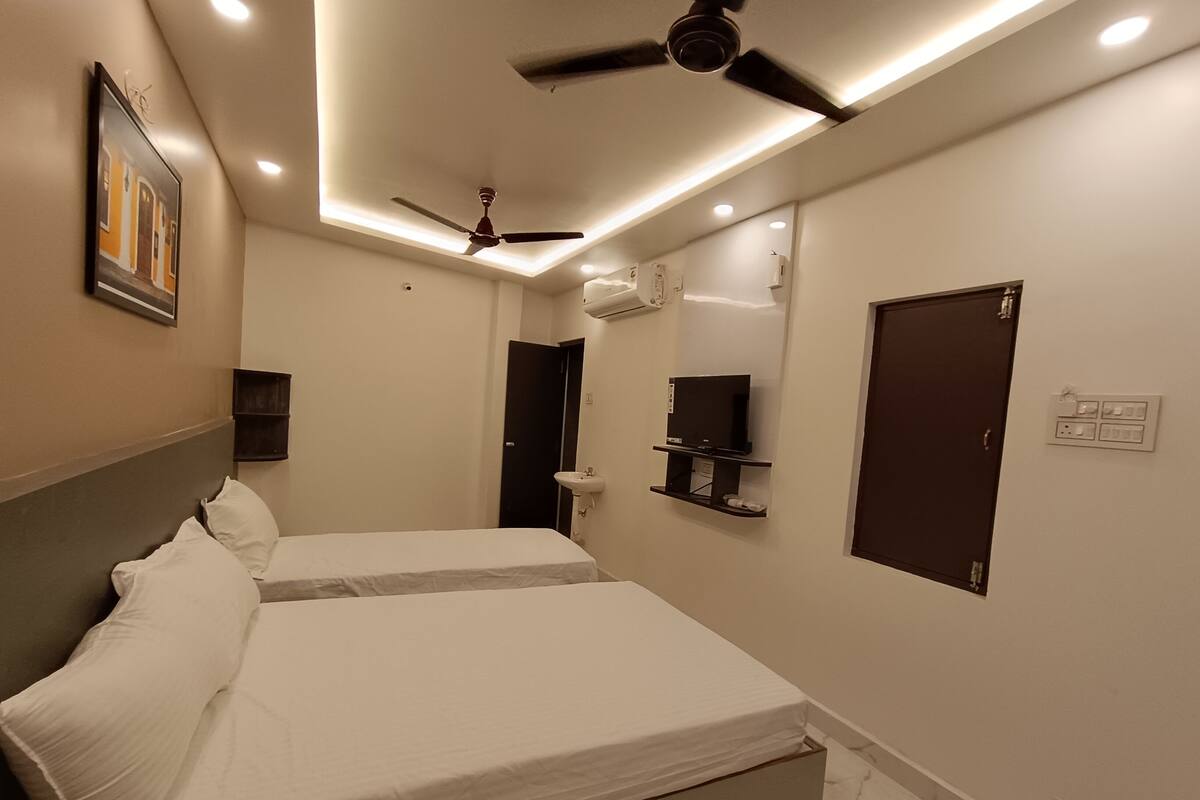A modern hotel room with a large bed, ceiling fan, built-in TV, and a small bathroom.