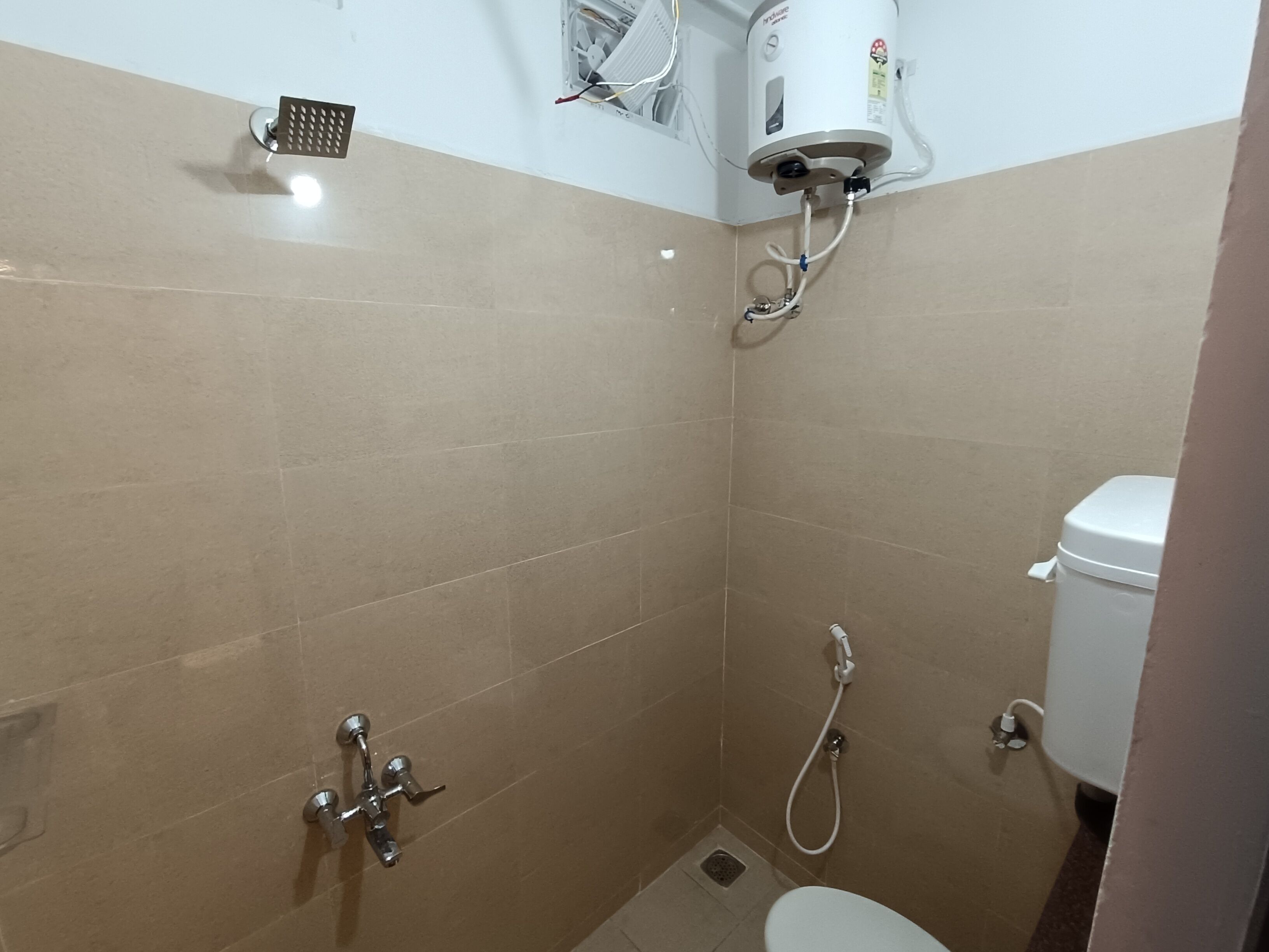 Une petite salle de bain carrelée, équipée d’une douche, de toilettes et d’un chauffe-eau.