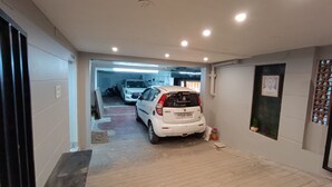 Un couloir étroit, avec une voiture blanche garée au fond, une moto visible au loin et une porte sur la gauche.