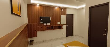 A modern hotel room with a wooden vanity, a flat-screen TV, a large bed, and a dark door.