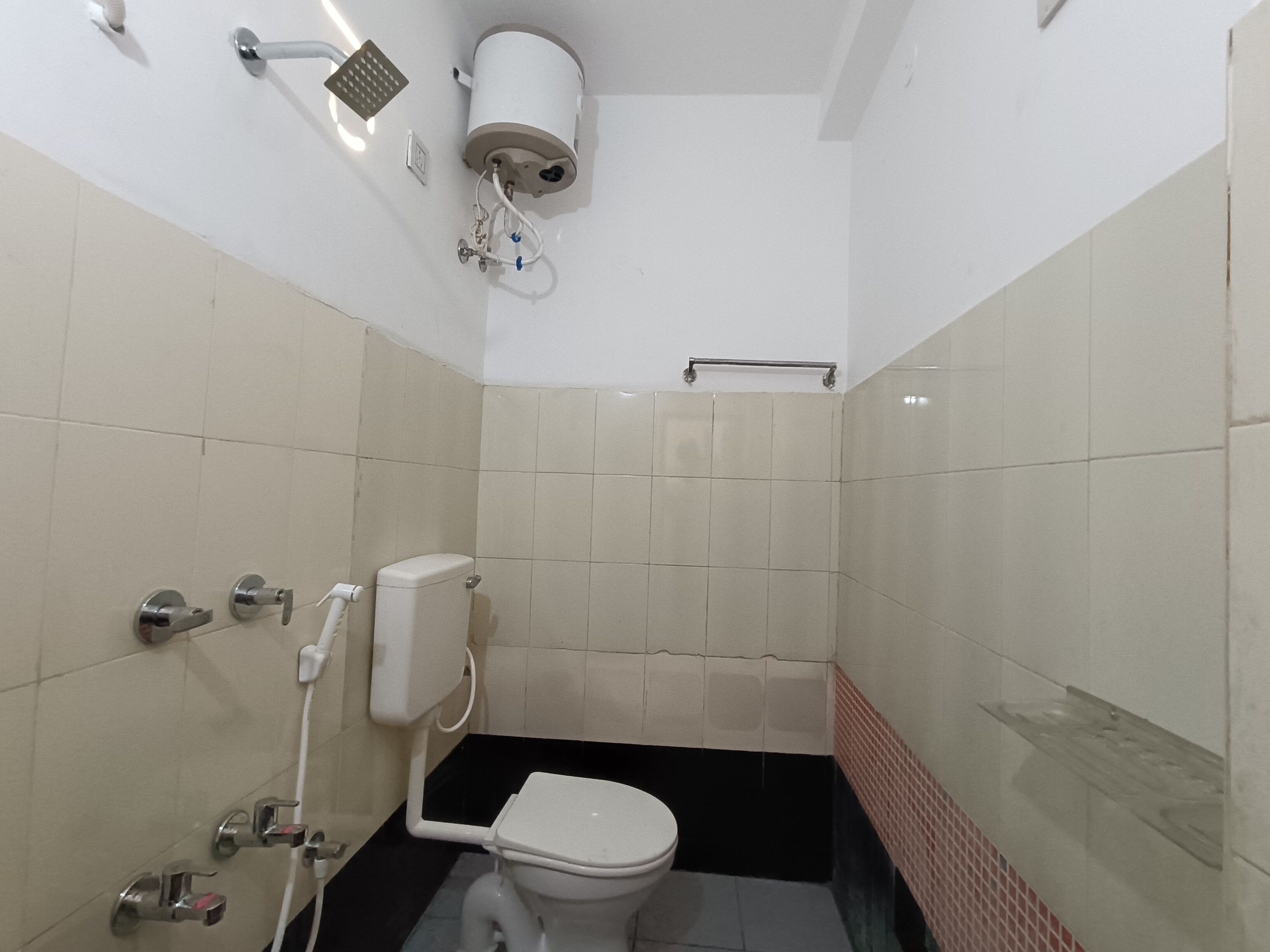Ein kleines Badezimmer mit Fliesen, Toilette, Dusche und Handtrockner.