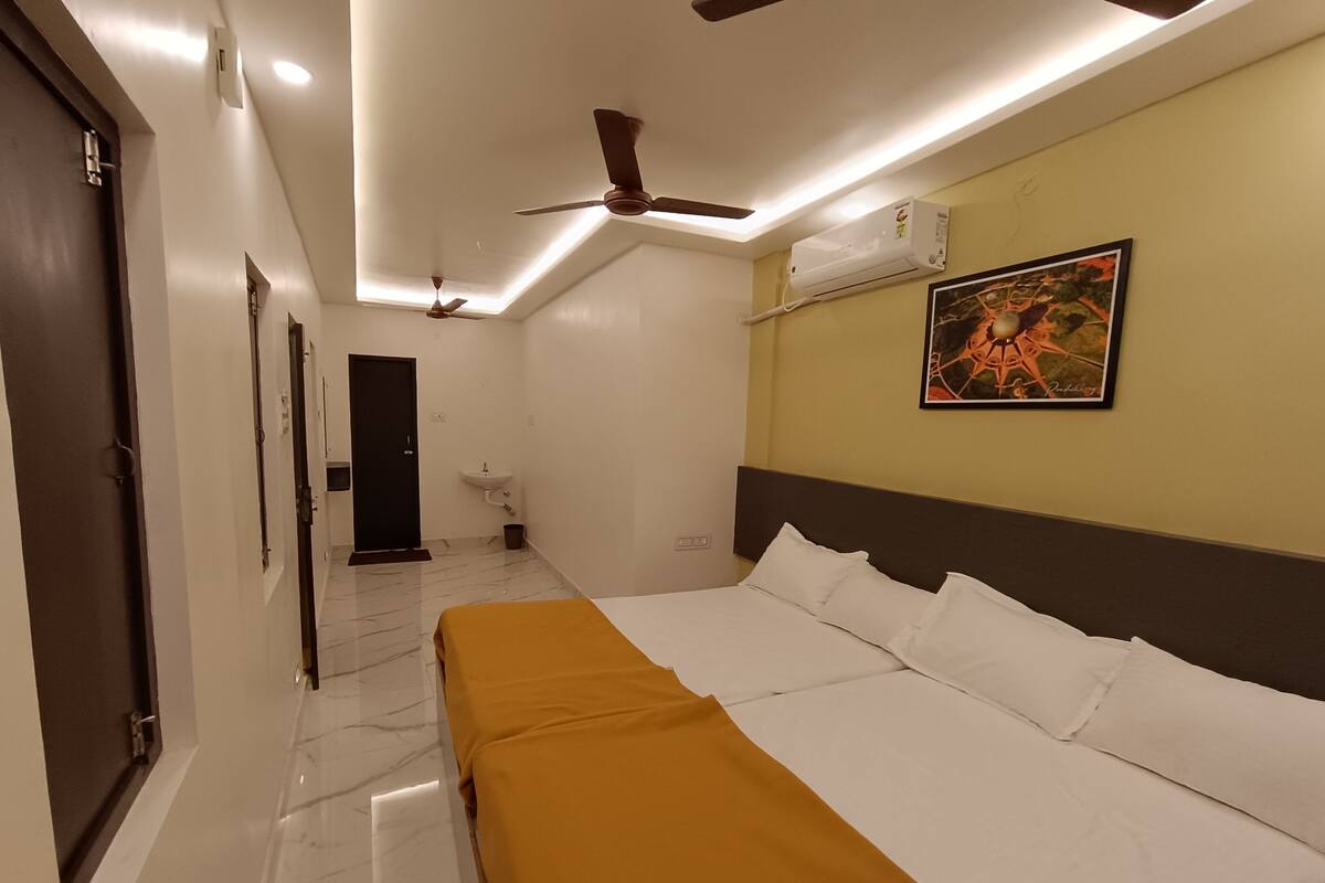 A hotel room with a bed, a ceiling fan, an air conditioning unit, a sink, and a door.