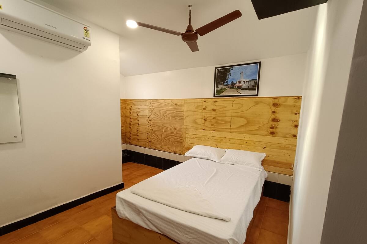 A bedroom with a wooden headboard, a bed with white bedding, a ceiling fan, and an air conditioning unit.