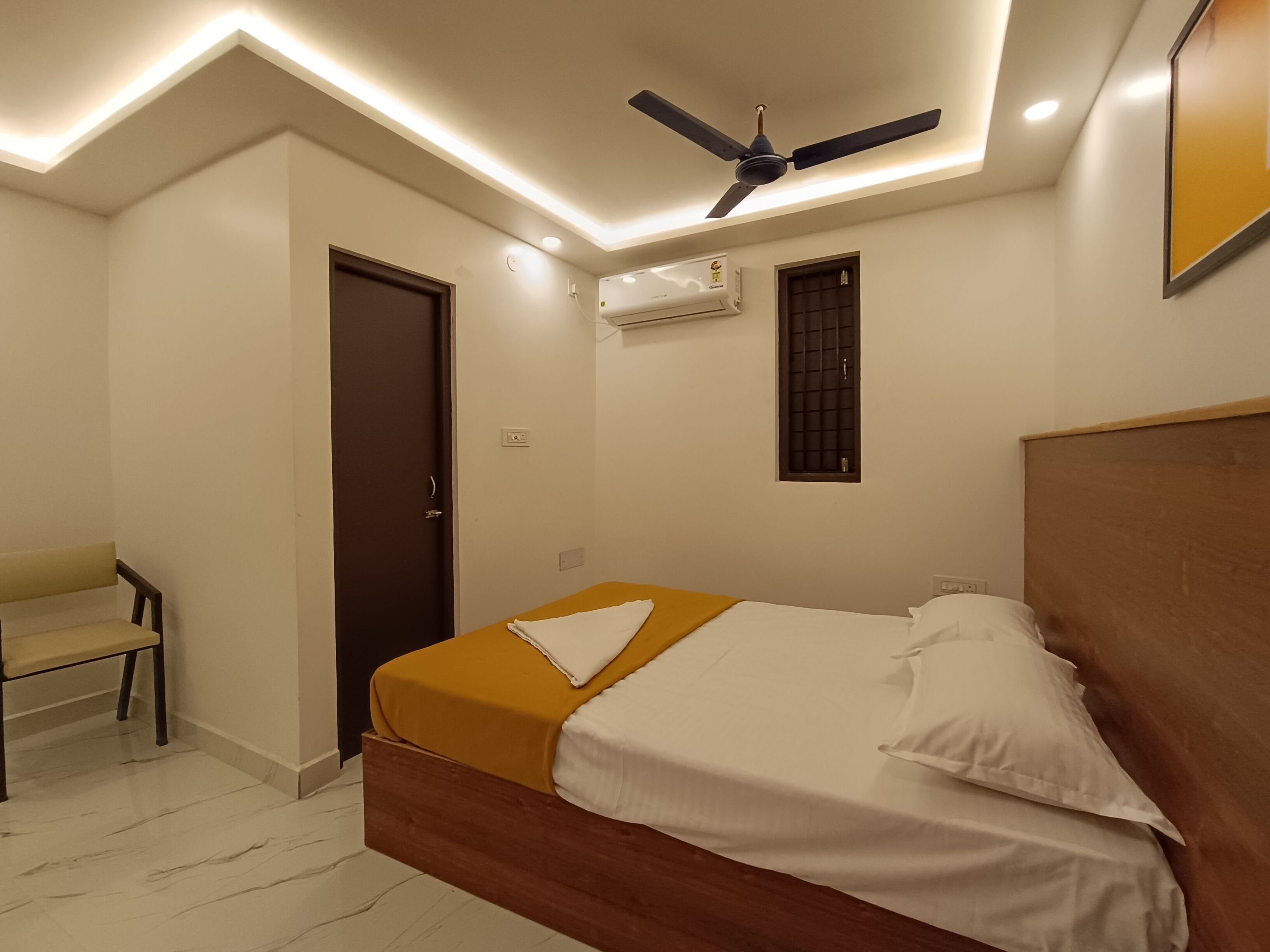 A bedroom with a bed, a ceiling fan, an air conditioning unit, a window, and a chair.