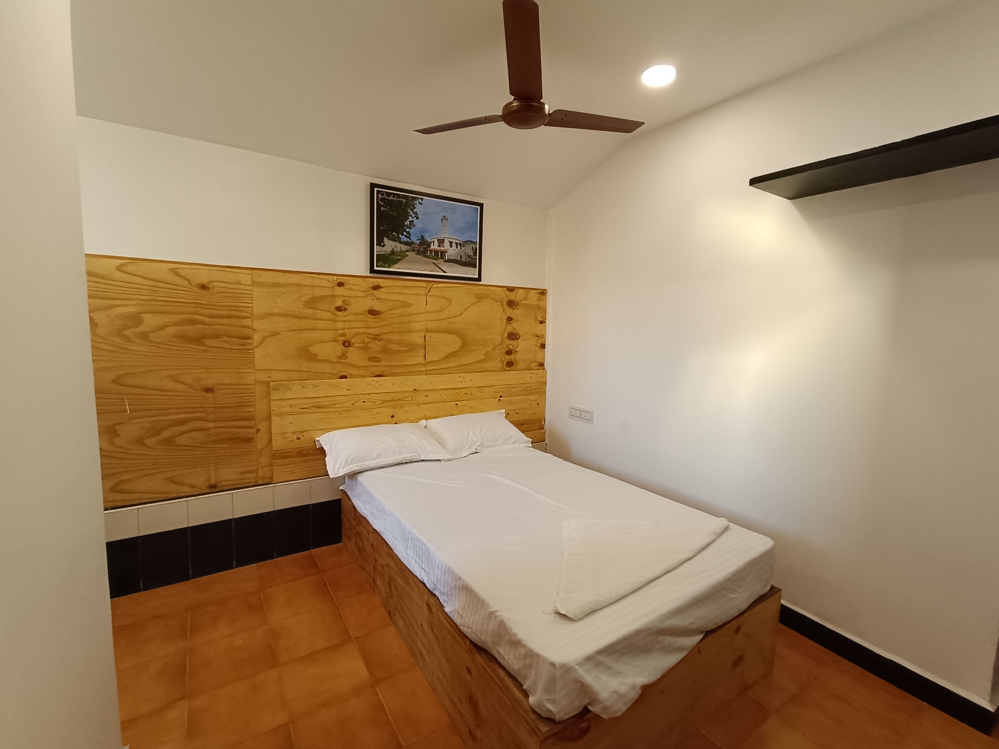 A bedroom with a wooden headboard, a single bed, a ceiling fan, and a framed picture on the wall.