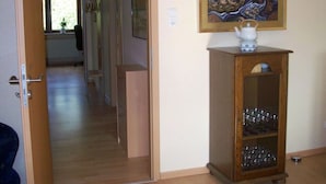Ein Flur mit einem Holzkabinett, das Gläser und eine Teekanne enthält, einem Gemälde an der Wand und einer Tür zu einem anderen Raum.
