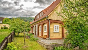 A traditional wooden house with a sloped roof, a stone foundation, and a wooden fence in the foreground.