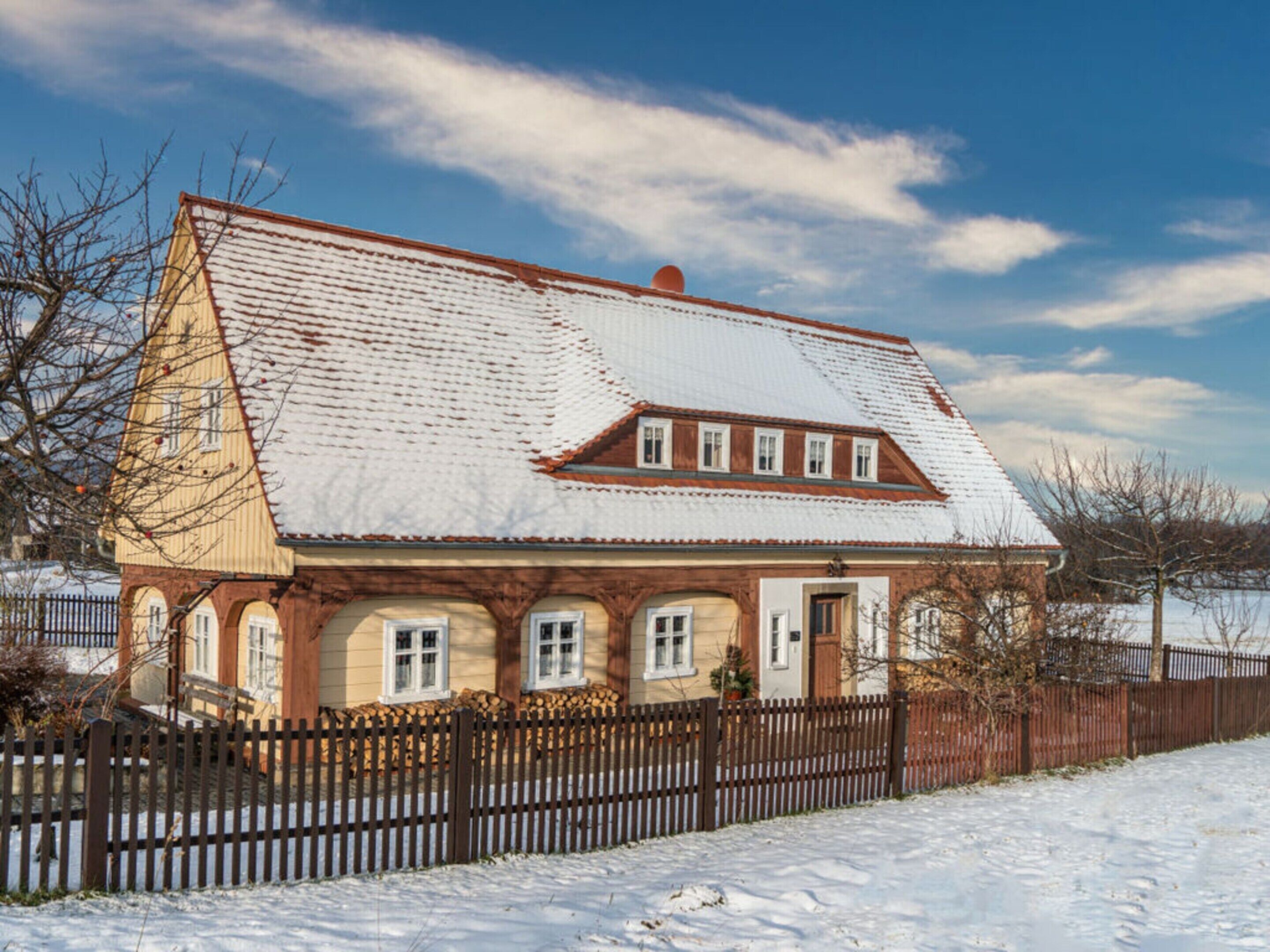 A traditional chalet with a sloped roof, wooden facade, and a fenced yard.