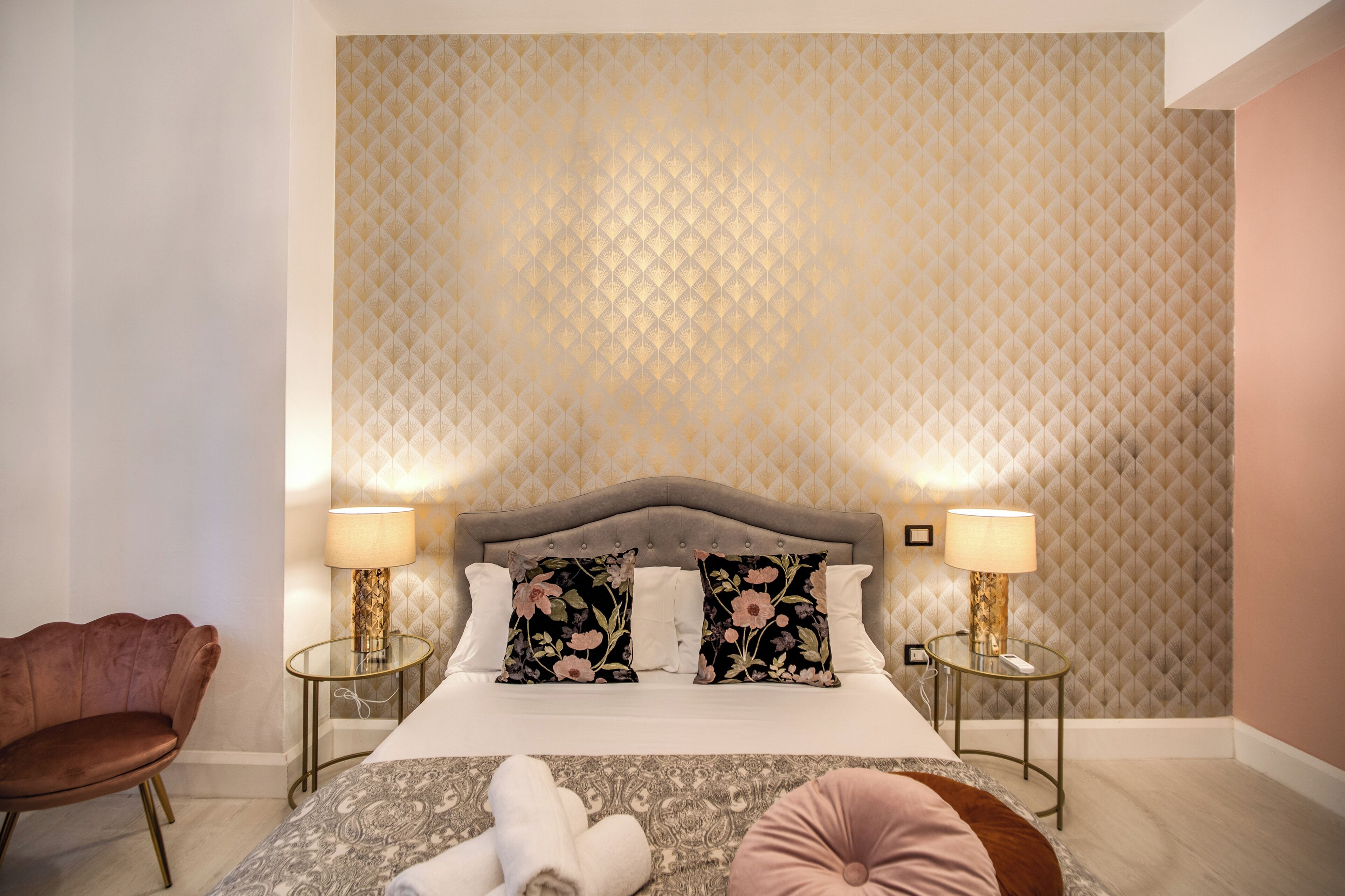 Ein Schlafzimmer mit einem großen Bett, zwei Nachttischen, einem Sessel und einer Wand mit Muster.