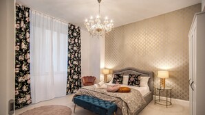 Een slaapkamer met een groot bed, een kroonluchter, een nachtkastje met een lamp en een bankje.