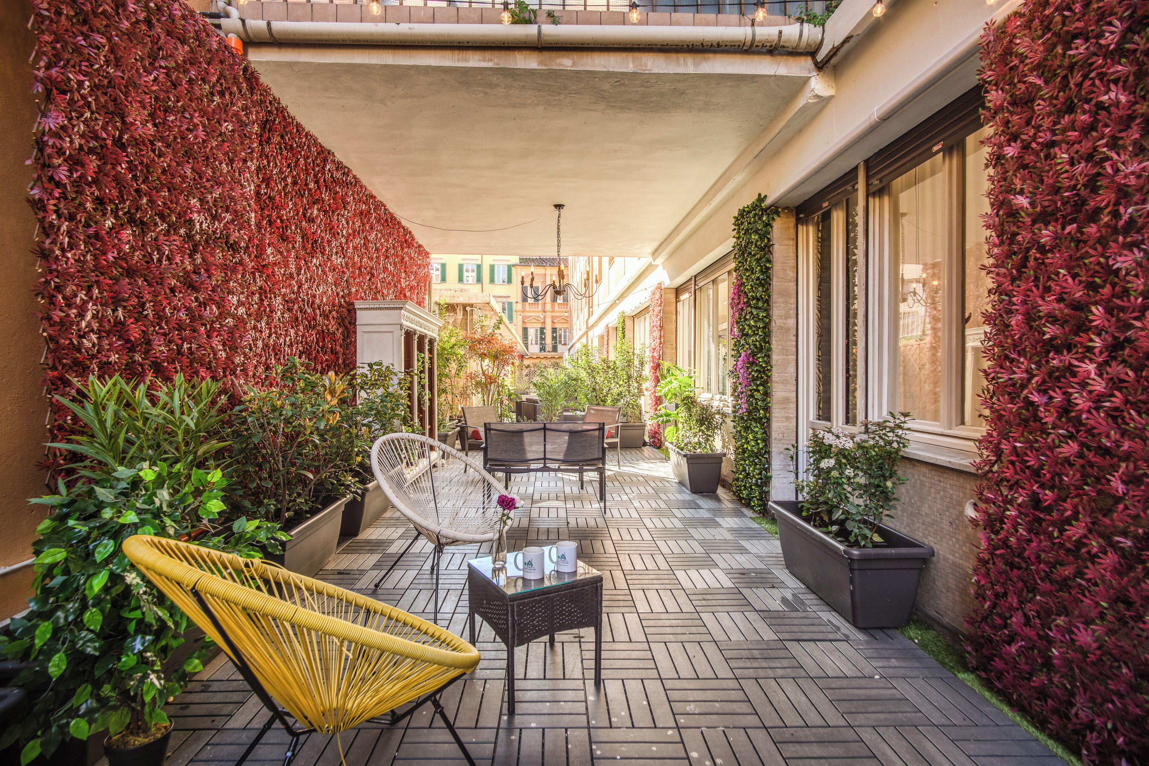 Un patio exterior cubierto con sillas de mimbre, una mesa y plantas en macetas.