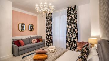 Una habitación de hotel moderna con un sofá gris, una cama con ropa de cama estampada, una araña y cortinas florales.