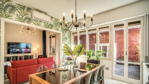 Een moderne woonkamer met een rode bank, een glazen eettafel en een televisie waarop 'Inventing Anna' wordt vertoond.