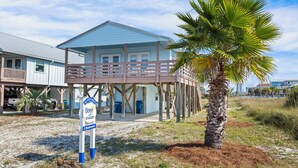 Une propriété de deux étages située en bord de mer, dotée d’une terrasse en bois et d’une pancarte indiquant qu’elle comprend deux chambres.