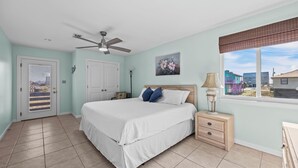 Une chambre à coucher comprenant un lit, une table de chevet, un ventilateur de plafond, une fenêtre avec vue et une porte dotée d’une fenêtre.