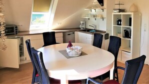 A compact kitchen with a dining area, featuring a round table, chairs, a built-in oven, and a coffee machine.