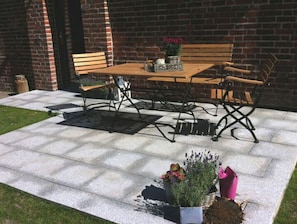A patio with a wooden table and metal chairs, surrounded by potted plants and a brick wall. - Ferienwohnung Altes Zollhaus Burgstaaken (Fehmarn)