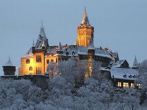 A historic castle with multiple towers and a prominent central tower, surrounded by snow-covered trees. - Am Lustgarten Modern Retreat (Wernigerode)