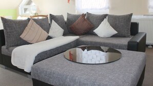 A modern living room with a grey sectional sofa, a glass coffee table, and a painting on the wall. - Am Lustgarten Modern Retreat (Wernigerode)