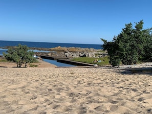 Ein Sandstrand mit einem kleinen Teich, Felsformationen und Bäumen.