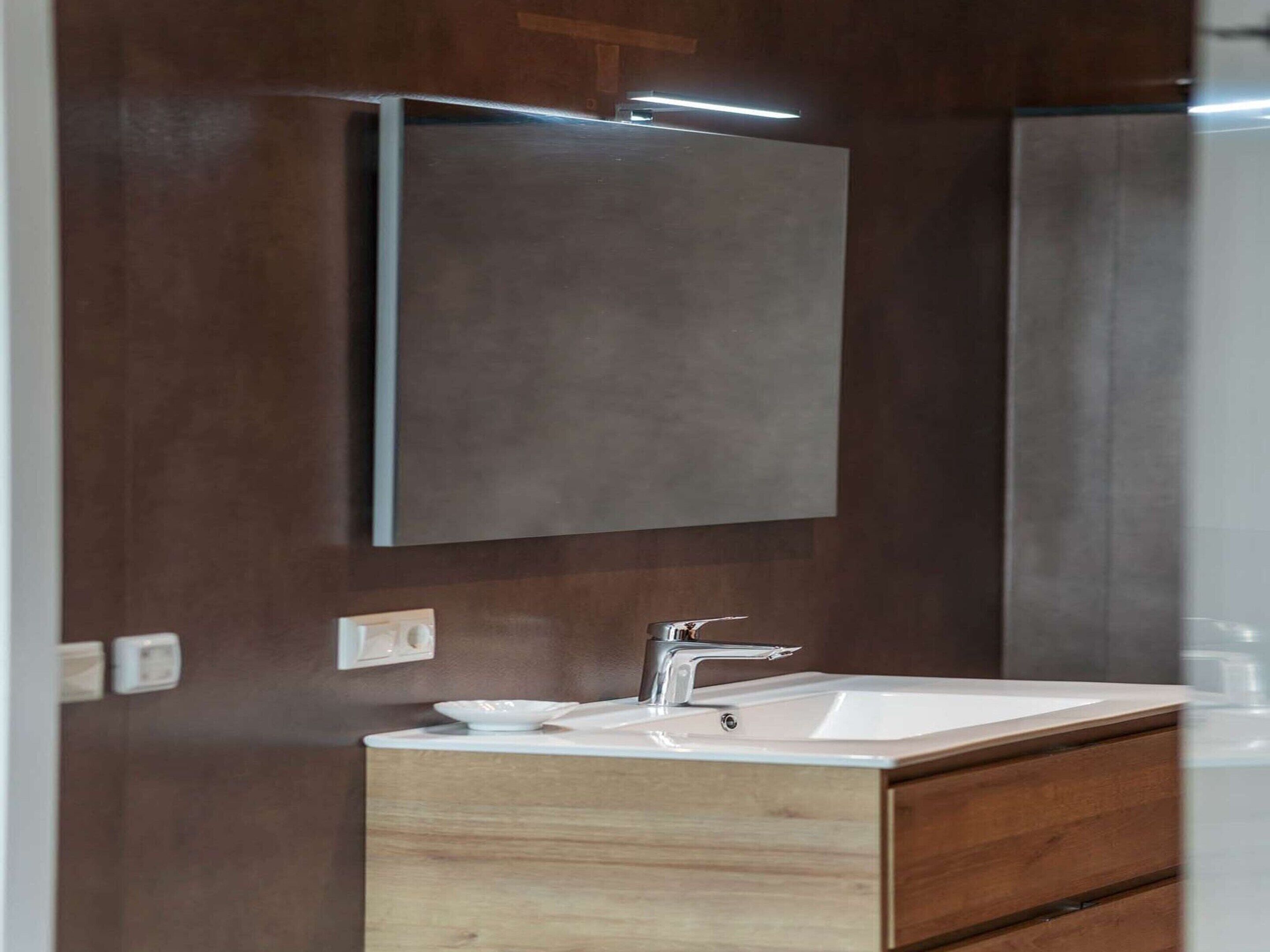 A modern bathroom with a wooden vanity, a white sink, and a large mirror.