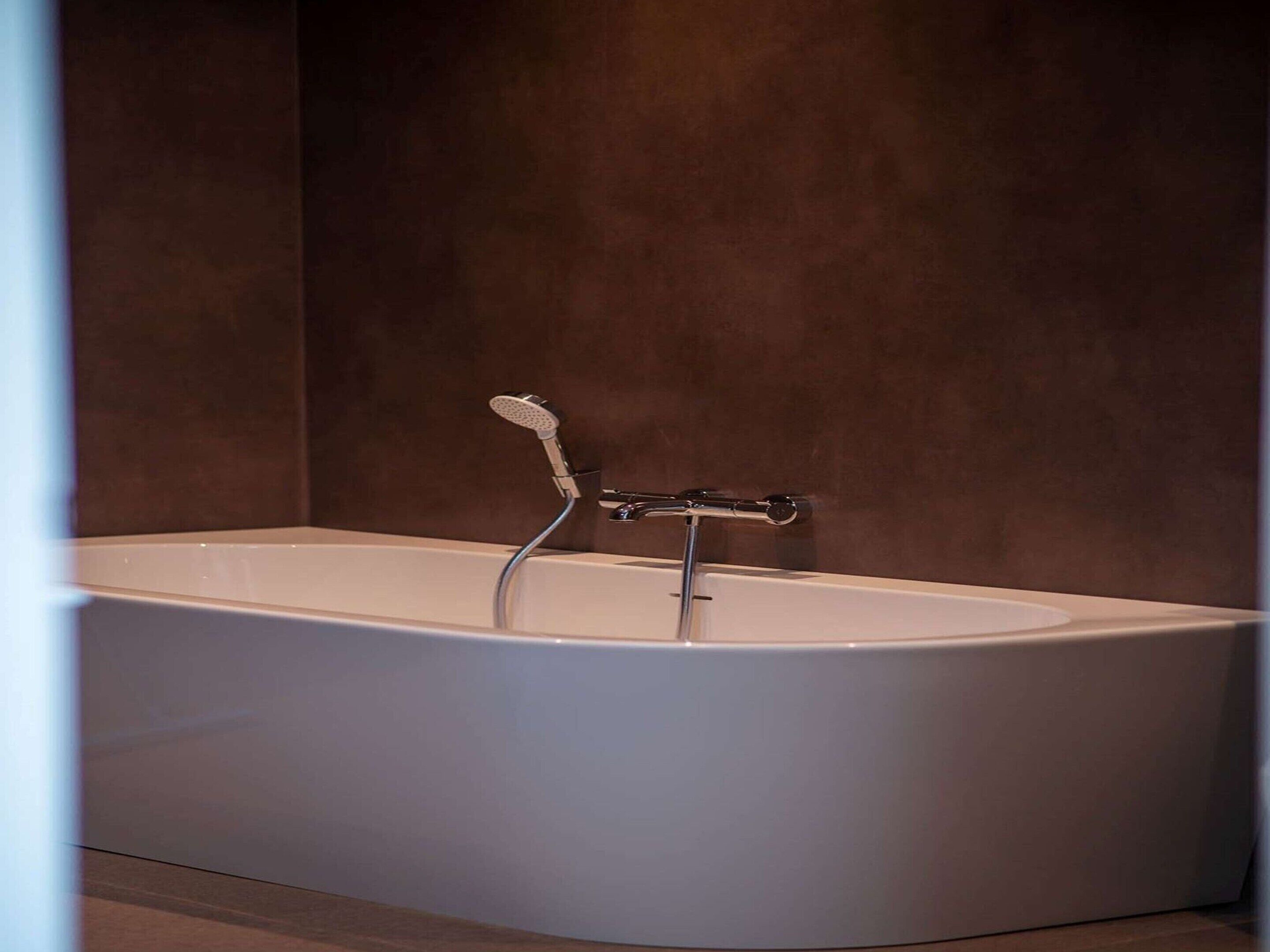 Una bañera moderna con cabezal de ducha manual en un baño con paredes marrón oscuro.