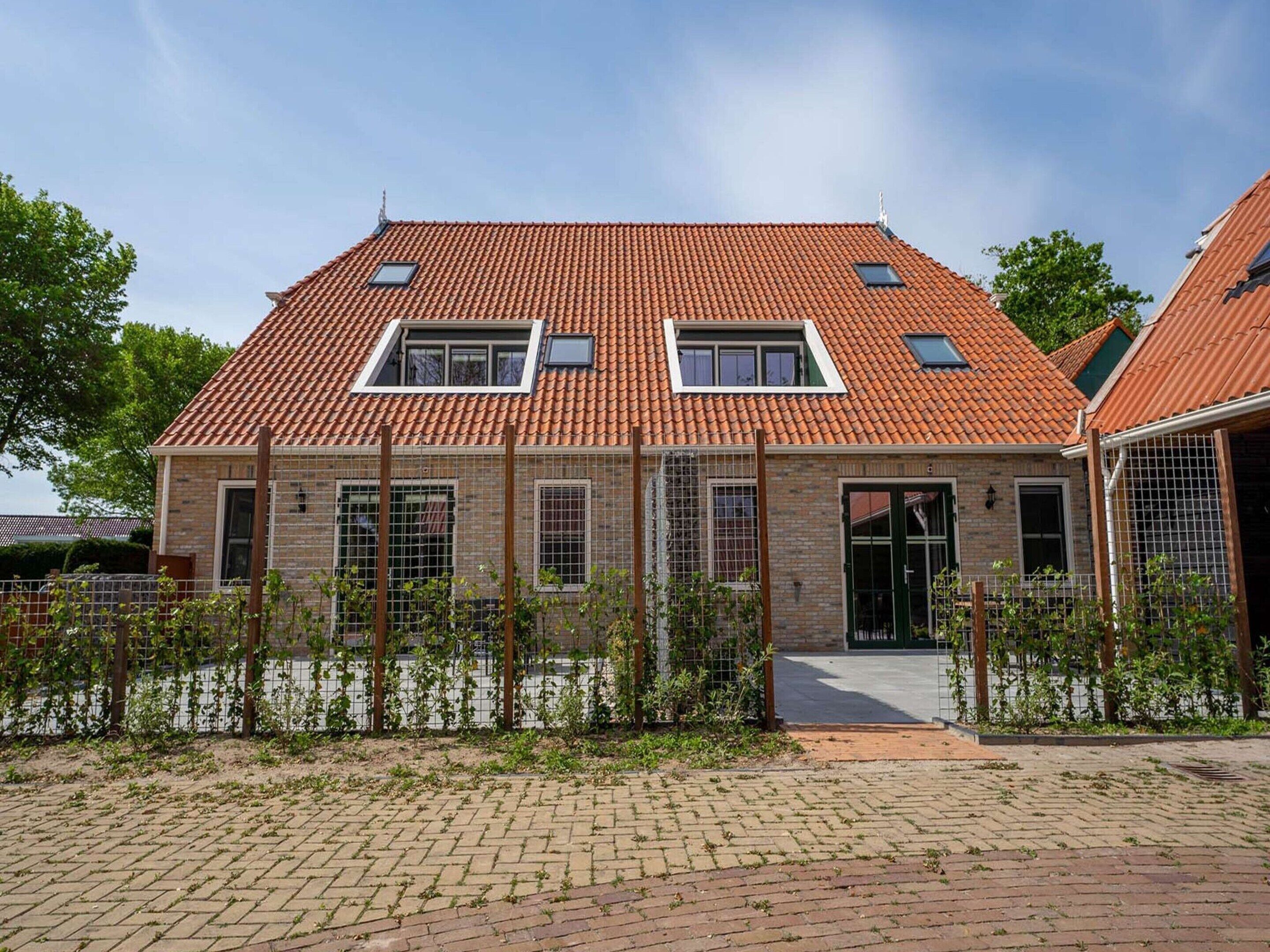 A two-story house with a tiled roof, a small garden, and a paved driveway.