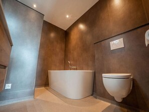 Une salle de bain moderne avec une baignoire sur pieds, des toilettes suspendues et un éclairage encastré au plafond.
