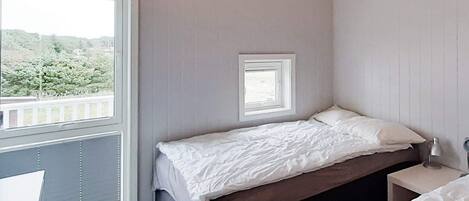 Une chambre avec un lit simple, une petite fenêtre et une table de chevet.
