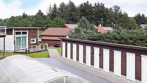 A modern building with a greenhouse structure, a brick wall with white doors, and a red-roofed building in the background. - 4 Person Holiday Home in Farsund (Farsund)