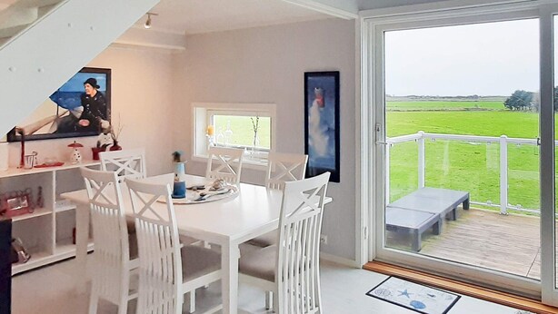 A dining area with a white table and chairs, a staircase, and a view of a green field through a glass door. - 4 Person Holiday Home in Farsund (Farsund)