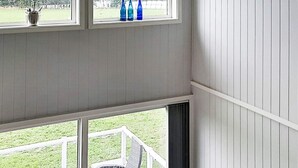 A room with a balcony, a window with blue bottles, and a view of a grassy area. - 4 Person Holiday Home in Farsund (Farsund)