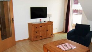 A living room with a wooden cabinet, a television, a lamp, and a dark blue armchair. - "jadestrasse" 40 Merchant (Wangerland)