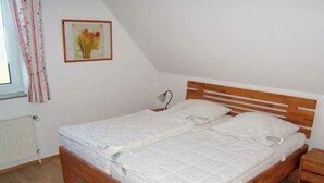 A single-bed room with a wooden headboard, a bedside table, a radiator, and a window with curtains. - "jadestrasse" 40 Merchant (Wangerland)